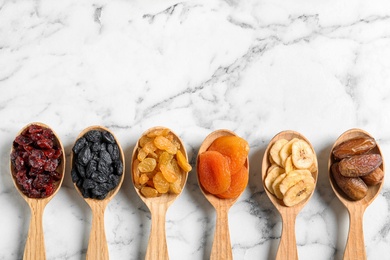 Photo of Spoons of different dried fruits on marble background, top view with space for text. Healthy lifestyle