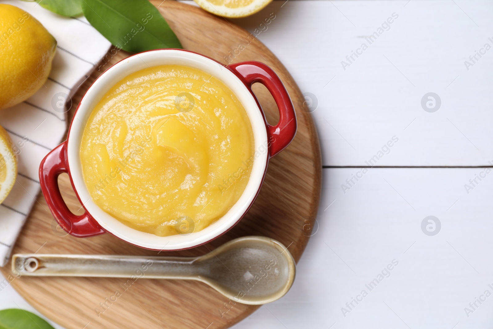 Photo of Delicious lemon curd in bowl, fresh citrus fruits and spoon on white wooden table, flat lay. Space for text