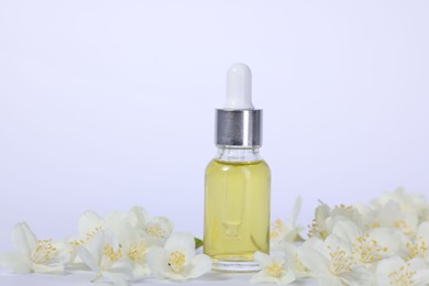 Photo of Essential oil in bottle and beautiful jasmine flowers on white background