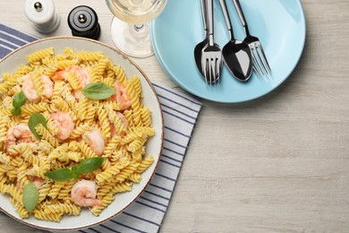 Delicious pasta with shrimps, basil and parmesan cheese served on light wooden table, flat lay