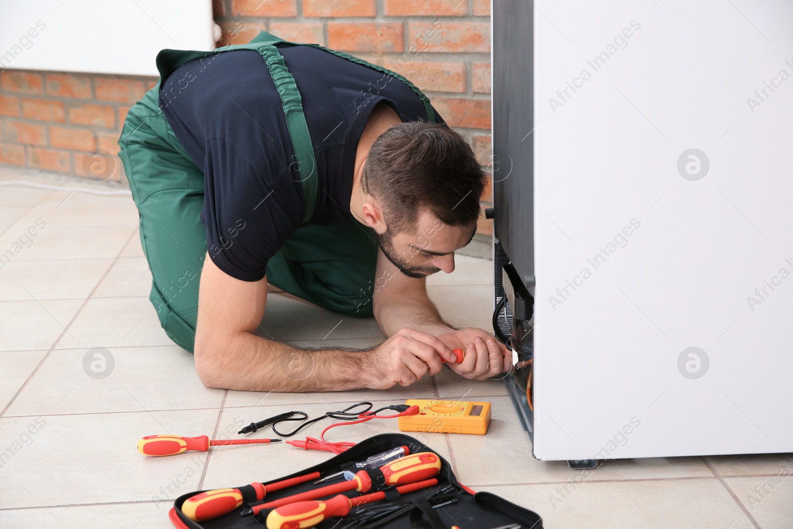 Photo of Male technician in uniform repairing refrigerator indoors