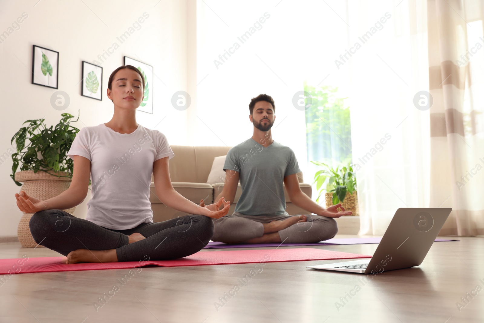 Photo of Couple practicing yoga while watching online class at home during coronavirus pandemic. Social distancing