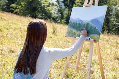 Photo of Young woman drawing on easel outdoors, back view
