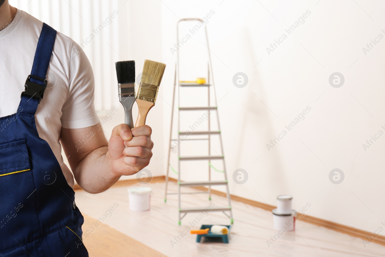 Photo of Male decorator with paint brushes in empty room, closeup. Space for text