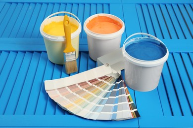 Photo of Buckets of paints, palette and brush on light blue wooden background