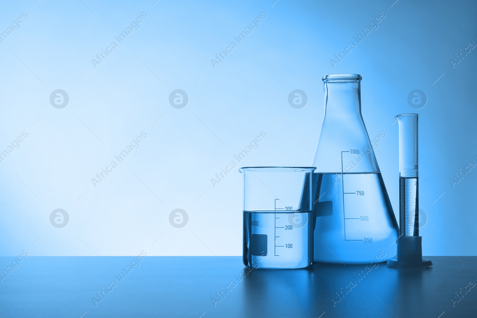 Image of Laboratory glassware with liquid on table, space for text. Toned in blue