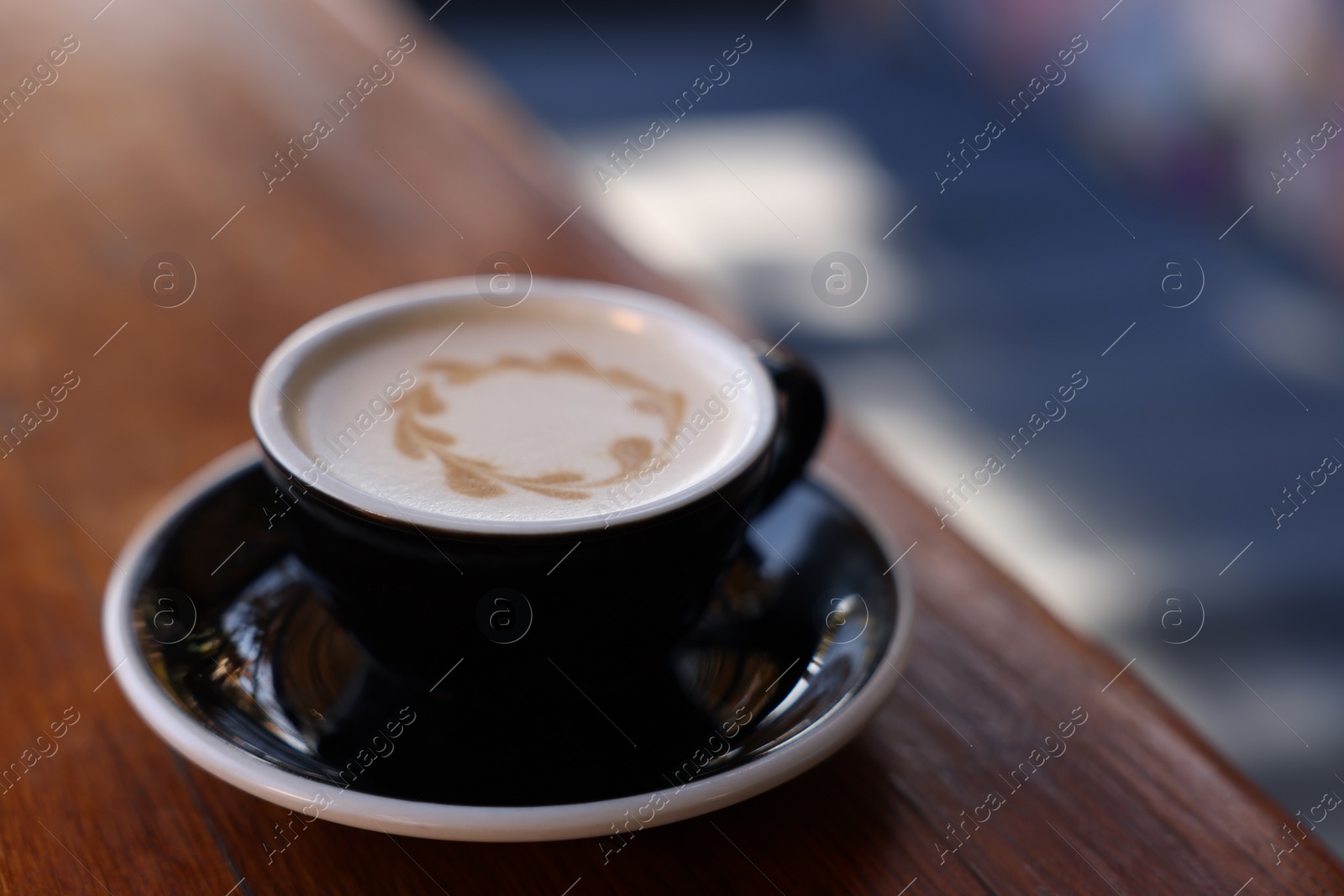 Photo of Ceramic cup of aromatic coffee with foam on wooden table in outdoor cafe. Space for text