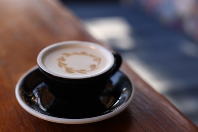 Ceramic cup of aromatic coffee with foam on wooden table in outdoor cafe. Space for text