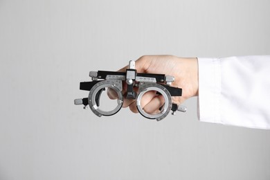 Photo of Ophthalmologist holding trial frame on light background, closeup