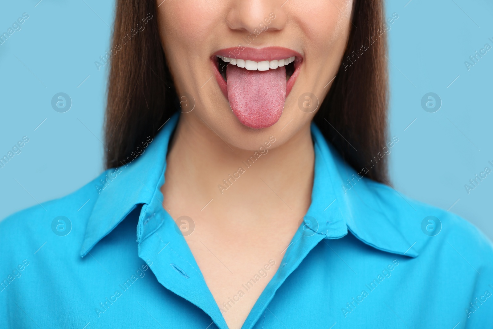 Photo of Woman showing her tongue on light blue background, closeup