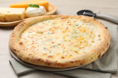 Photo of Delicious cheese pizza, cutter and different kinds of cheese on wooden table, closeup