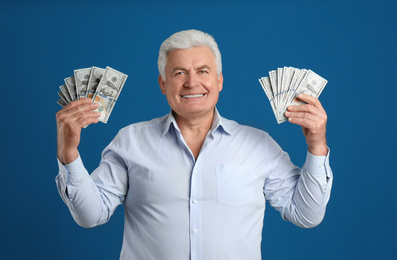Happy senior man with cash money on blue background