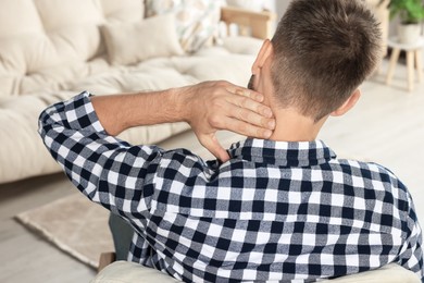Photo of Man suffering from neck pain indoors, back view