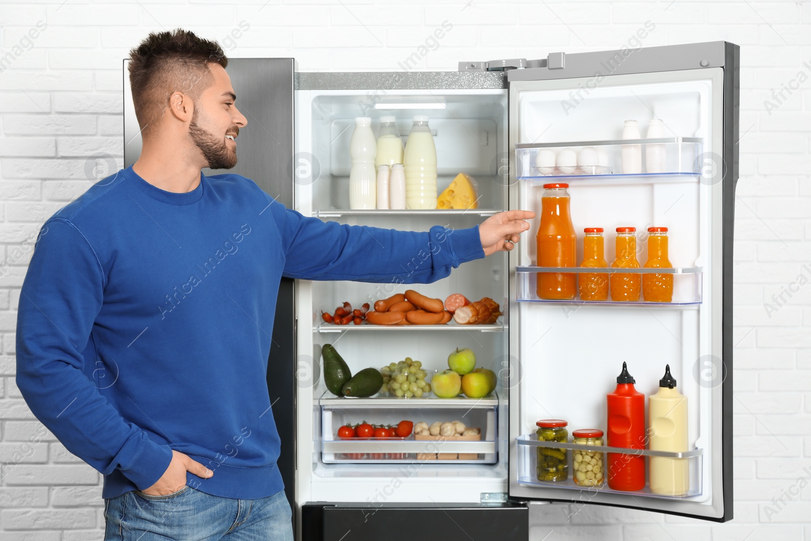 Photo of Young man taking juice out of refrigerator indoors