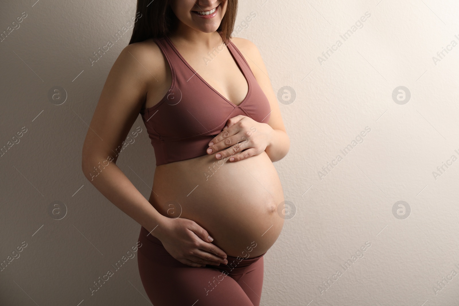 Photo of Pregnant young woman touching belly on beige background, closeup