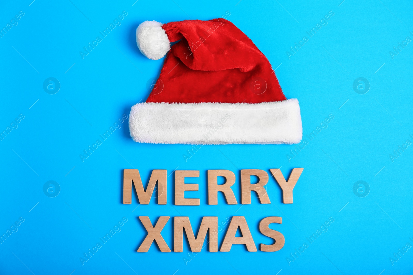 Photo of Santa Claus red hat and Merry Xmas made of wooden letters on color background, top view