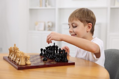 Cute little boy playing chess at table in room