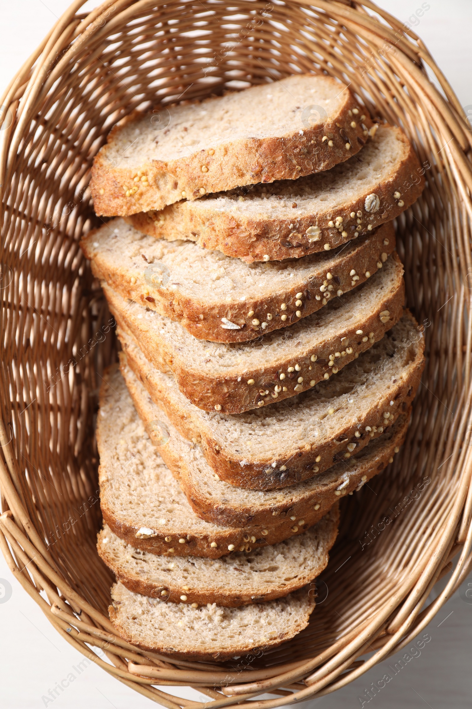 Photo of Slices of fresh homemade bread in wicker basket on white wooden table, top view