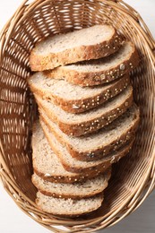 Slices of fresh homemade bread in wicker basket on white wooden table, top view