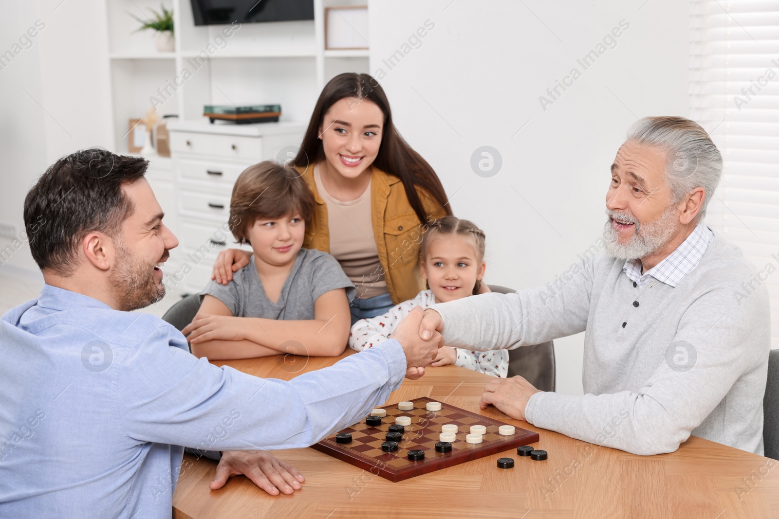 Photo of Happy family playing checkers at table in room