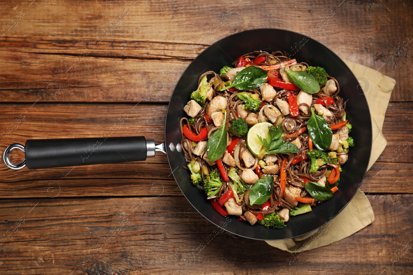 Photo of Stir-fry. Tasty noodles with meat and vegetables in wok on wooden table, top view