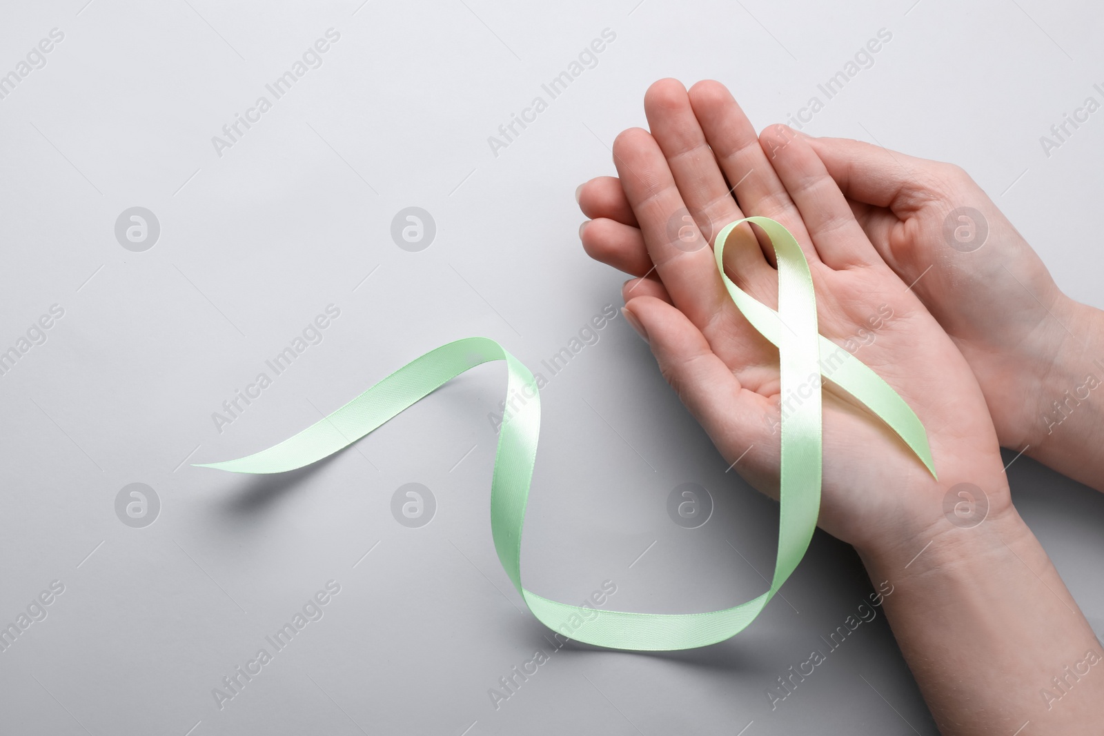 Photo of World Mental Health Day. Woman holding green ribbon on color background, top view