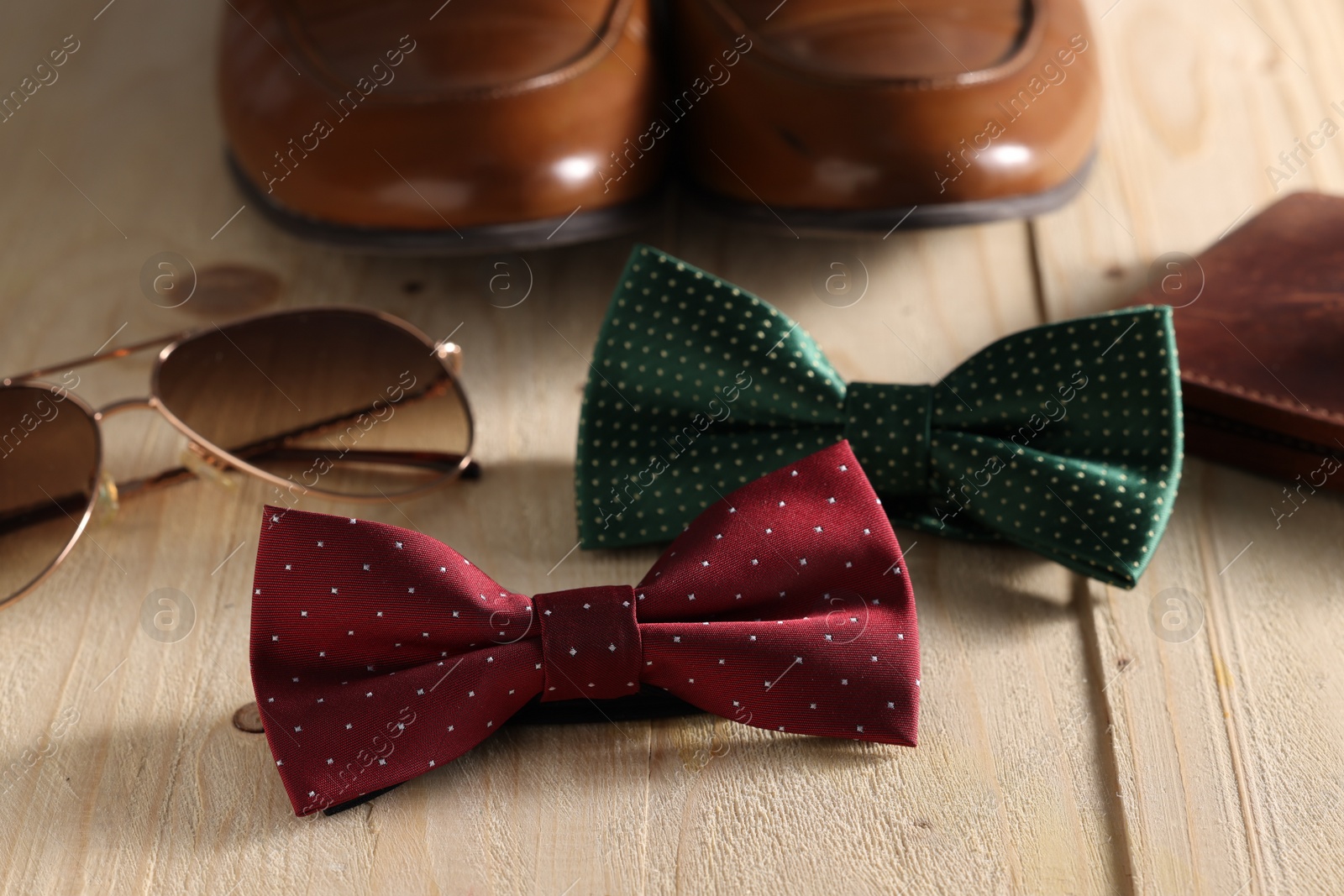 Photo of Stylish color bow ties and, sunglasses and shoes on wooden background