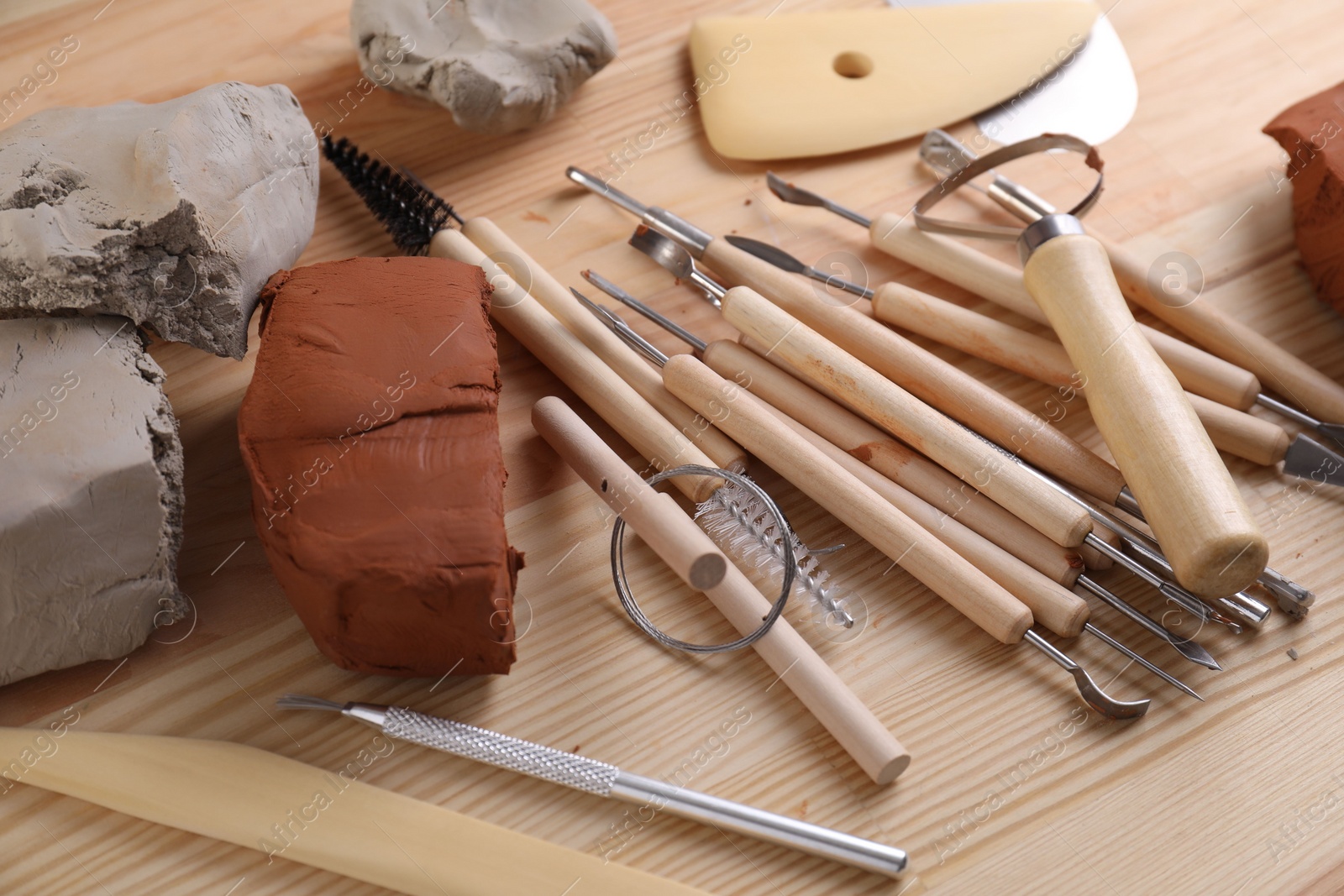 Photo of Clay and set of modeling tools on wooden table, closeup