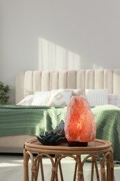 Beautiful Himalayan salt lamp and lotus figures on wicker table in bedroom, space for text