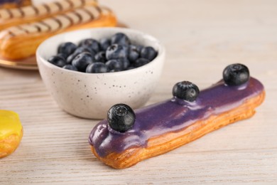 Photo of Tasty glazed eclair with blueberries on light wooden table, closeup