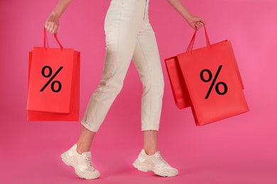 Image of Discount, sale, offer. Woman holding paper bags with percent signs against pink background, closeup