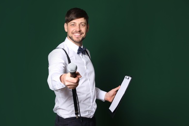 Handsome man in formal clothes with microphone and clipboard on color background. Space for text