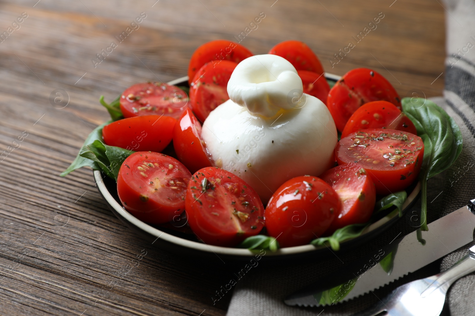 Photo of Delicious burrata cheese with tomatoes and basil served on wooden table, closeup