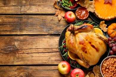 Photo of Traditional Thanksgiving day feast with delicious cooked turkey and other seasonal dishes served on wooden table, flat lay. Space for text