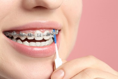 Photo of Smiling woman with dental braces cleaning teeth using interdental brush on pink background, closeup