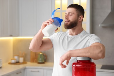 Young man with shaker of protein and powder at white marble table in kitchen