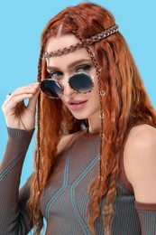 Photo of Stylish young hippie woman in sunglasses on light blue background