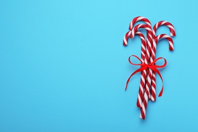 Photo of Sweet Christmas candy canes with red bow on light blue background, top view. Space for text