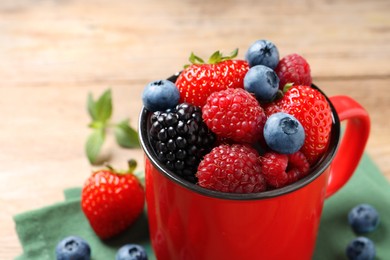 Photo of Many different fresh ripe berries in mug on wooden table, closeup. Space for text