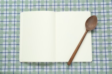Photo of Blank recipe book and wooden spoon on checkered tablecloth, top view. Space for text