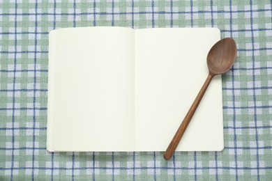 Blank recipe book and wooden spoon on checkered tablecloth, top view. Space for text