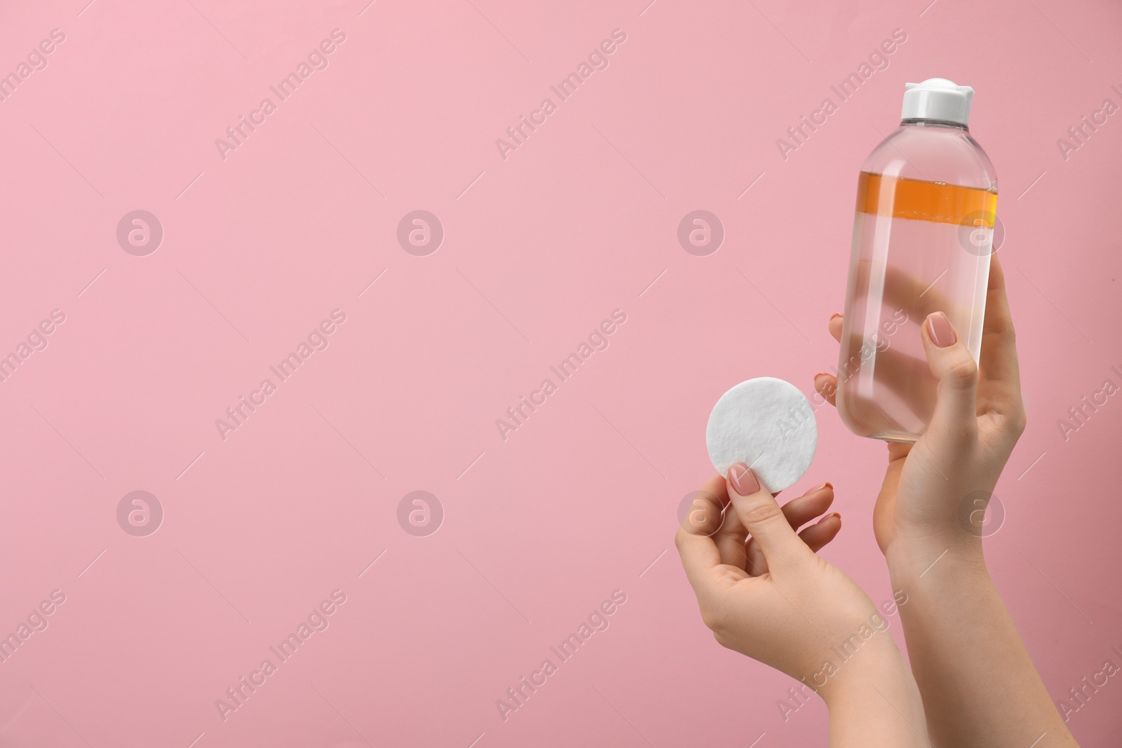 Photo of Woman holding makeup remover and cotton pad on pink background, closeup. Space for text