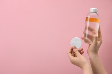 Woman holding makeup remover and cotton pad on pink background, closeup. Space for text