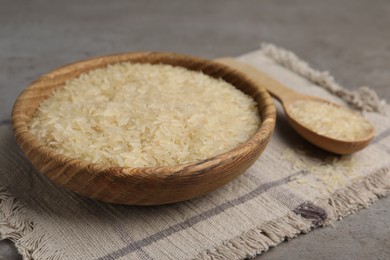 Bowl and spoon of raw rice on grey table, closeup