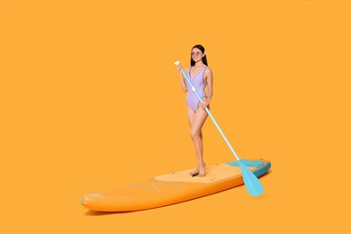 Happy woman with paddle on SUP board against orange background