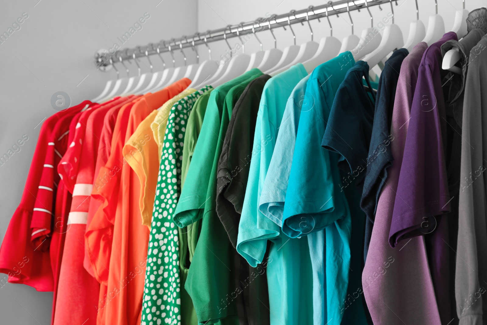 Photo of Hangers with different colorful clothes on rack in wardrobe