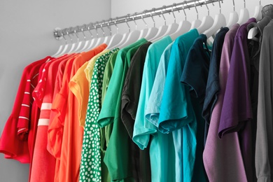 Photo of Hangers with different colorful clothes on rack in wardrobe