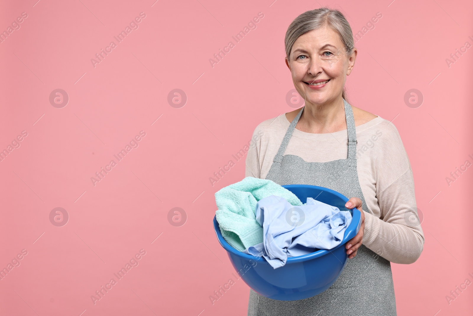 Photo of Happy housewife with basin full of laundry on pink background, space for text