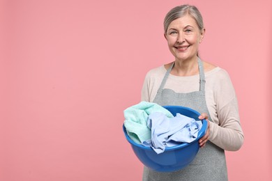 Photo of Happy housewife with basin full of laundry on pink background, space for text
