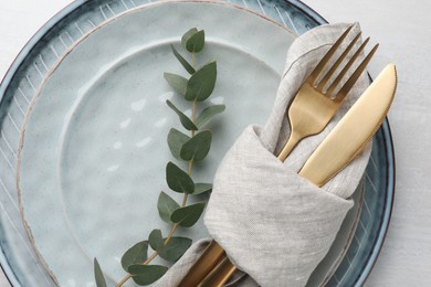 Photo of Stylish setting with cutlery, napkin, eucalyptus branch and plates on white table, top view